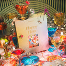 Colorful Happy Hour jigsaw puzzle box surrounded by vibrant cocktail glasses, disco ball, and festive party decorations
