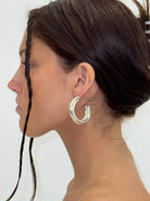 Silver chunky triple twist hoop earrings worn by model with dark hair in updo, shown in profile view