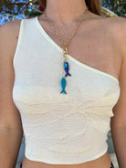 Gold chain necklace with blue enamel fish charms and lobster clasp, modeled on white ribbed tank top