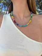 Colorful multicolored gemstone beaded necklace with small round stones in rainbow hues worn on woman's neck
