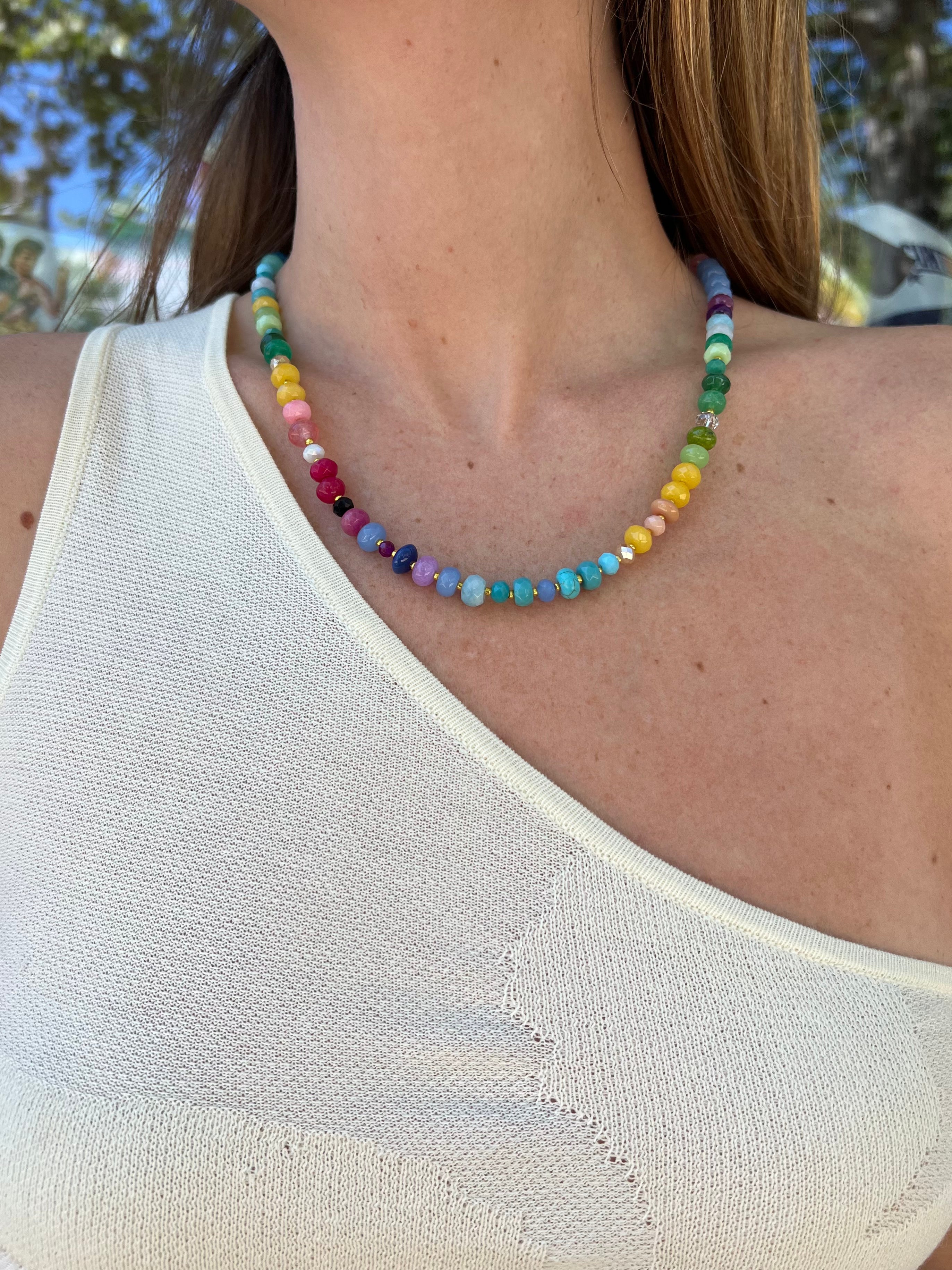 Colorful multicolored gemstone beaded necklace with small round stones in rainbow hues worn on woman's neck