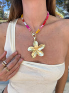 Colorful beaded necklace with gold flower pendant and toggle clasp, featuring pink, red, yellow, and white glass beads