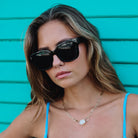 Woman wearing sunglasses and a blue top against a turquoise background