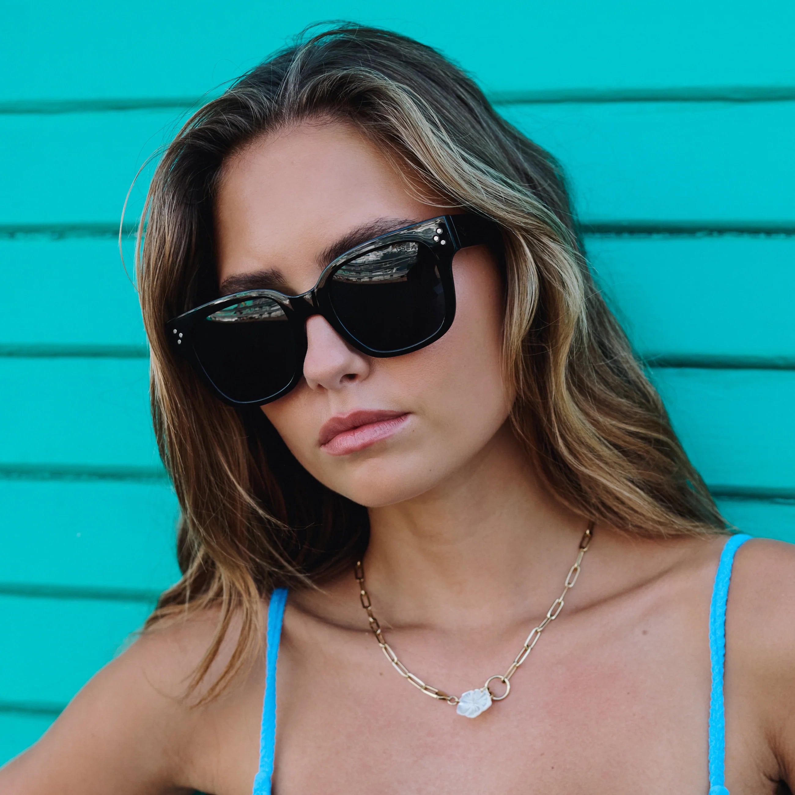 Woman wearing sunglasses and a blue top against a turquoise background