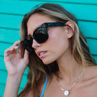 Woman wearing sunglasses and a blue bikini top against a teal background