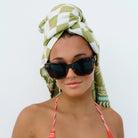 Woman wearing sunglasses and a green and white patterned headscarf on a plain background