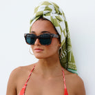 Woman wearing sunglasses and a green headscarf with a white pattern on a plain background