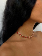 Gold necklace with oval red coral gemstones set in bezel frames, worn on neck with black hair visible