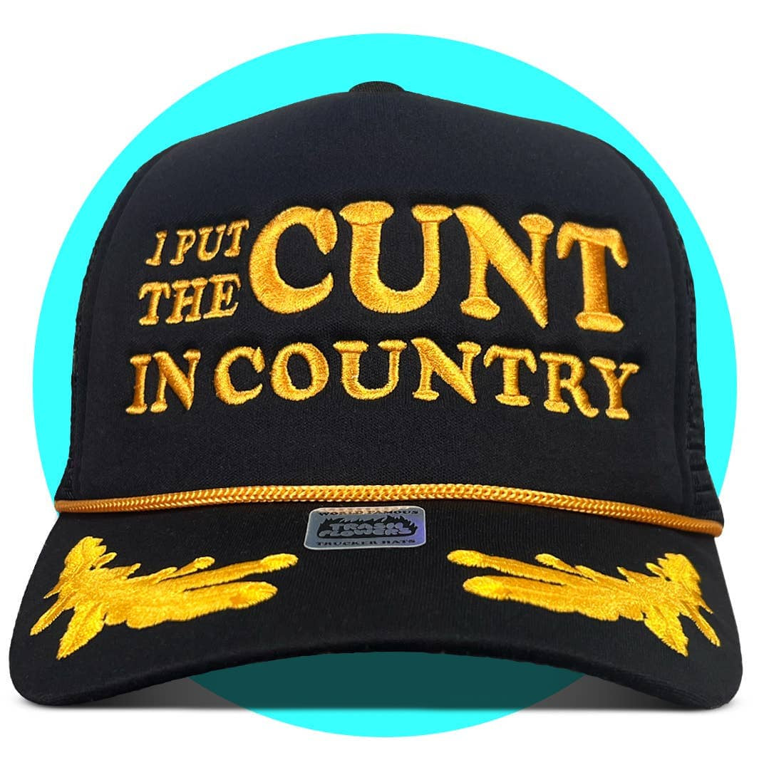 Black trucker hat with gold embroidered text "I PUT THE CUNT IN COUNTRY" and decorative leaf design on brim