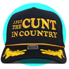 Black trucker hat with gold embroidered text "I PUT THE CUNT IN COUNTRY" and decorative leaf design on brim