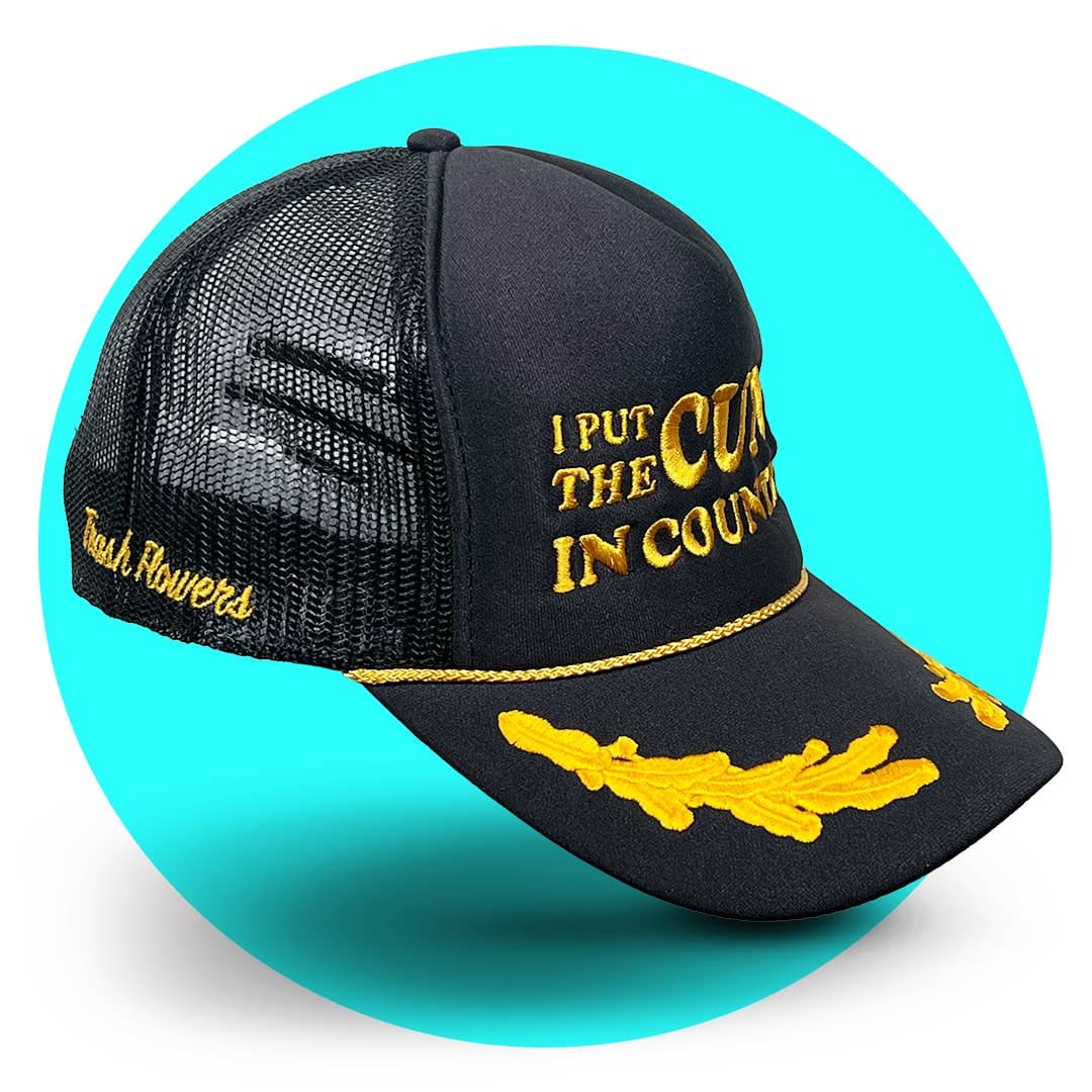 Black mesh trucker hat with gold embroidery reading "I PUT THE CUNT IN COUNTRY" and decorative rope trim on brim