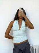 Mint green halter neck top with ruched V-neckline and fitted waist, worn with dark gray low-rise trousers