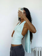 Light blue halter wrap top with ruched detailing and long draping ties, paired with gray trousers