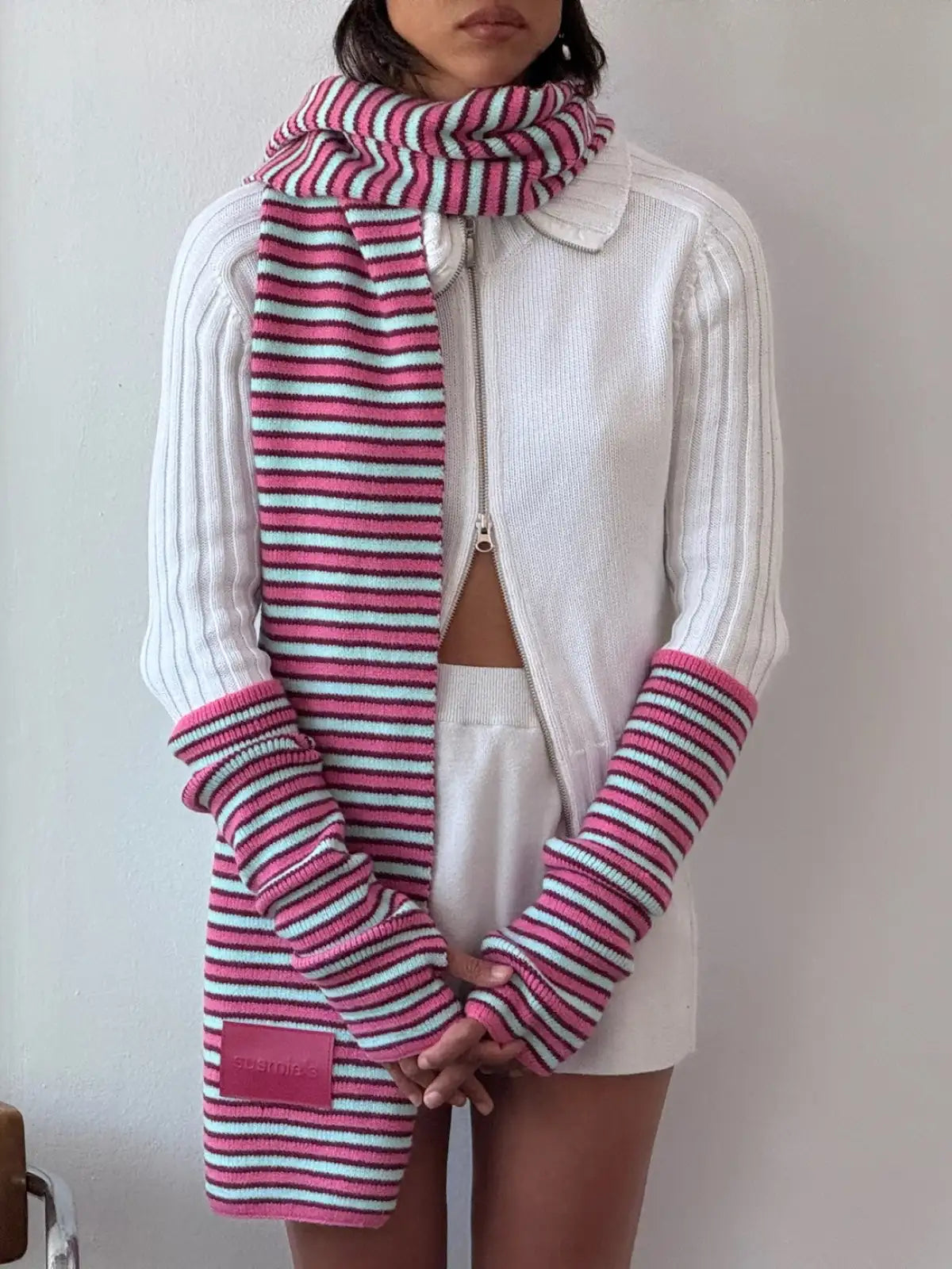 Pink, white, and turquoise striped knit scarf with matching ribbed sleeve warmers worn with white zip-up cardigan