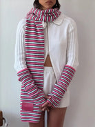 Pink, white, and turquoise striped knit scarf with matching ribbed sleeve warmers worn with white zip-up cardigan