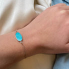 Delicate gold chain bracelet with oval turquoise stone centerpiece on wrist against white fabric background