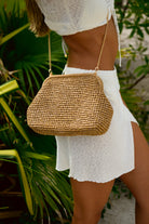 Person wearing a white dress and straw handbag with a tropical background