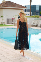 Woman in a black lace dress and hat by a pool with buildings in the background