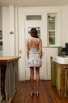 Woman wearing grey striped linen shorts and matching open-back crop top with tie closure, standing in rustic kitchen