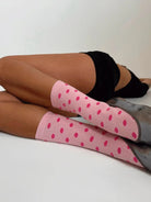 Pink polka dot knee-high socks with gray soles on crossed legs, worn with black athletic wear