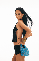 Blue beaded mini handbag with floral pattern and cutout handles, held against black sequined outfit with leopard print cuff