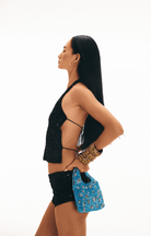 Woman in profile wearing black sequined outfit holding blue beaded bag and leopard print clutch against white background