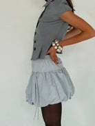 Light blue structured vest with button details paired with matching bubble hem mini skirt and pearl bracelet