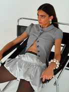 Gray button-front cropped shirt with collar and short sleeves, styled with matching mini skirt featuring gathered waist detail