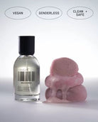 Clear glass bottle with black cap next to pink foam hair rollers, labeled vegan, genderless, and clean + safe