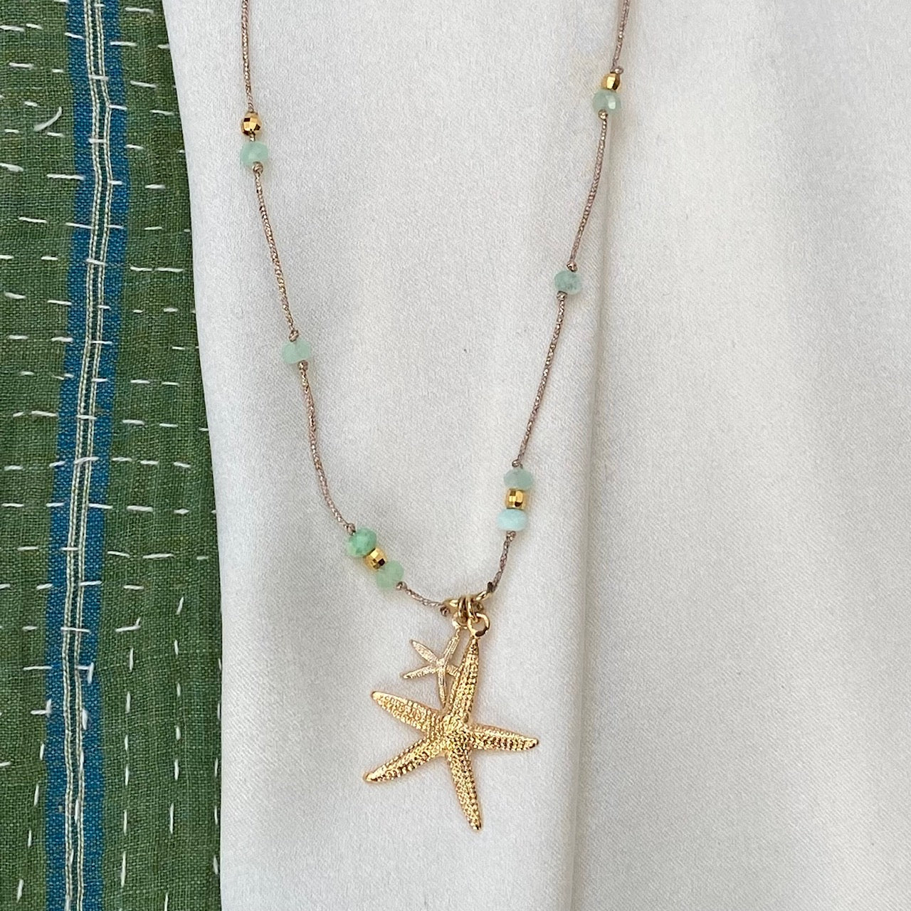 Gold starfish pendant necklace with light blue beads on rose gold chain displayed on white fabric background