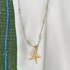 Gold starfish pendant necklace with light blue beads on rose gold chain displayed on white fabric background