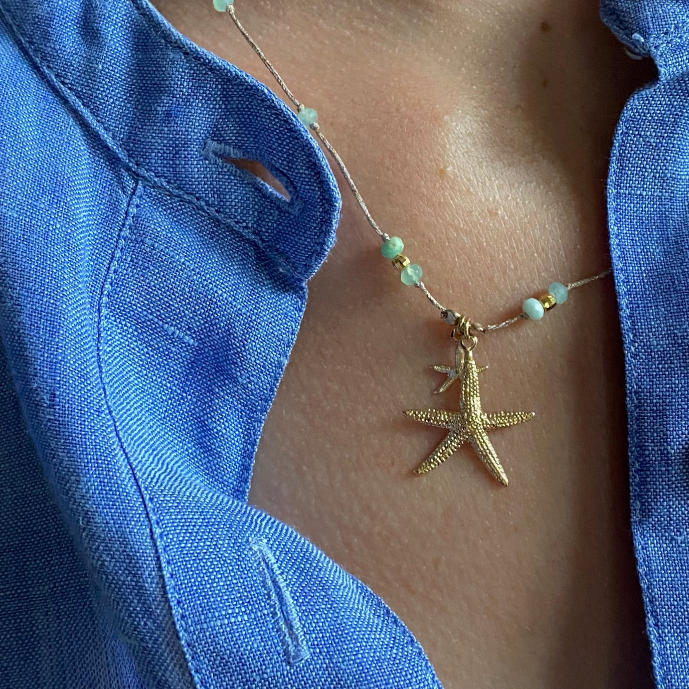 Gold starfish pendant necklace with turquoise beads on delicate chain worn against blue linen top
