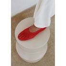 Red crocheted slip-on shoe with black beaded detail on white circular platform pedestal