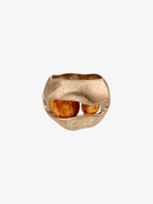 Gold sculptural ring with organic wavy design holding orange-brown wooden beads in the center opening