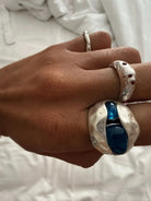 Hand wearing three hammered silver rings with blue and red gemstone accents against white fabric background