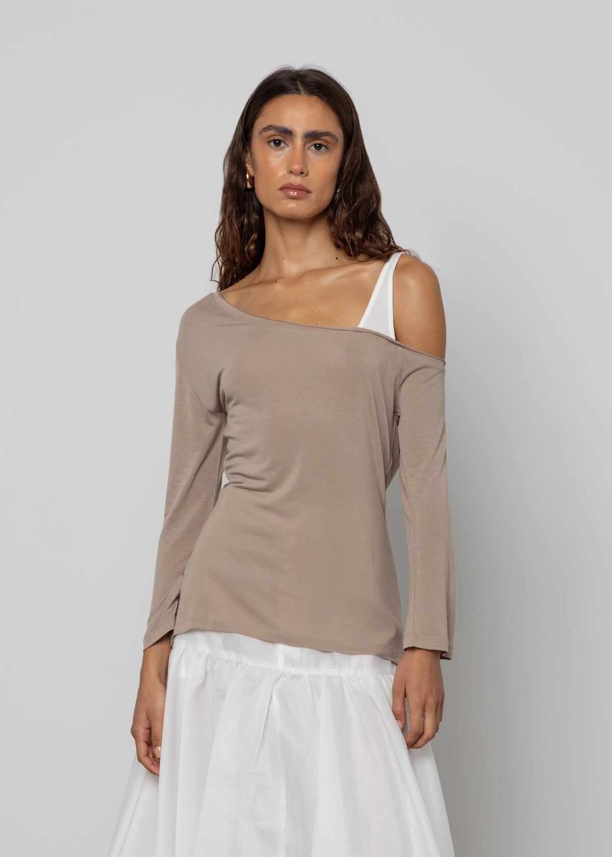 Taupe asymmetric off-shoulder long-sleeve top with white bra strap detail, styled with a white midi skirt.