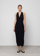 Black sleeveless midi wrap dress with textured fabric, V-neckline, and side tie detail worn with embellished sandals