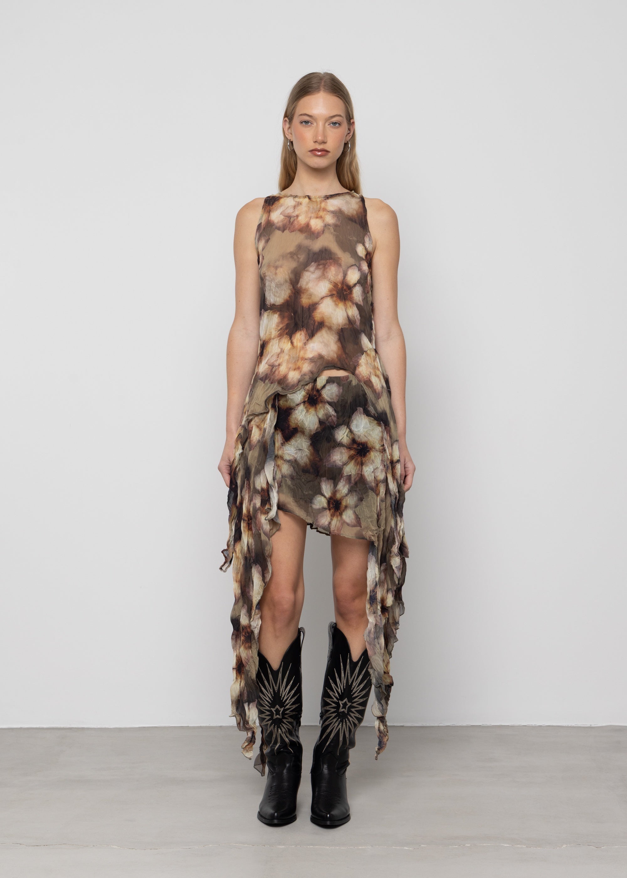Sleeveless tie-dye dress in brown and cream tones with asymmetric ruffled hem, worn with black embroidered cowboy boots