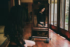 Woman in black outfit sitting in traditional Japanese room doorway with wooden floors and natural lighting