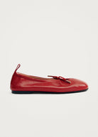 Red leather ballet flat with bow detail and gold metal tip accent, featuring a rounded toe and thin dark sole.