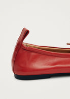 Red leather ballet flat with gold hardware detail, pull tab at heel, and dark rubber sole.