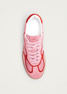 Pink and red suede sneaker with white laces viewed from above on beige background