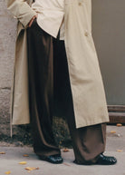 Person wearing black wide-leg pants with beige trench coat and black leather shoes on urban street