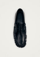 Black leather loafer with penny strap detail and moccasin stitching, viewed from above on light background