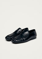 Black leather loafers with woven detail at toe and penny strap across vamp on beige background