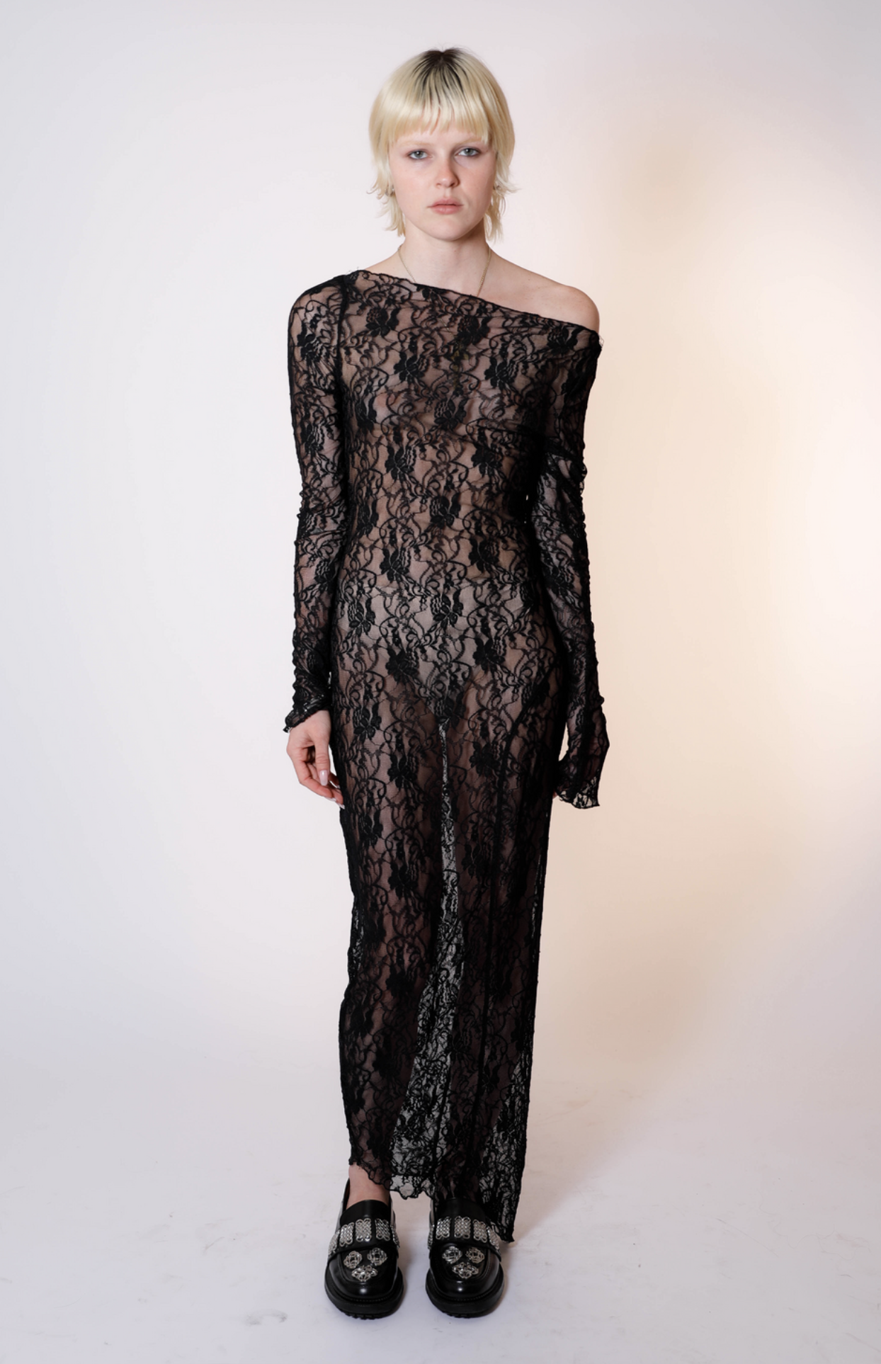 Black lace off-shoulder maxi dress with long sleeves and sheer floral pattern, worn with embellished loafers
