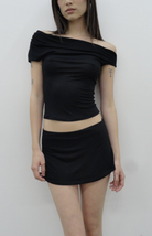 Black off-shoulder crop top and mini skirt set in stretchy fabric, worn by model with tattoos against white background