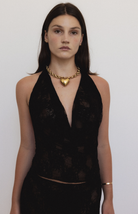 Gold chain necklace with heart pendant worn with black halter top on model against white background