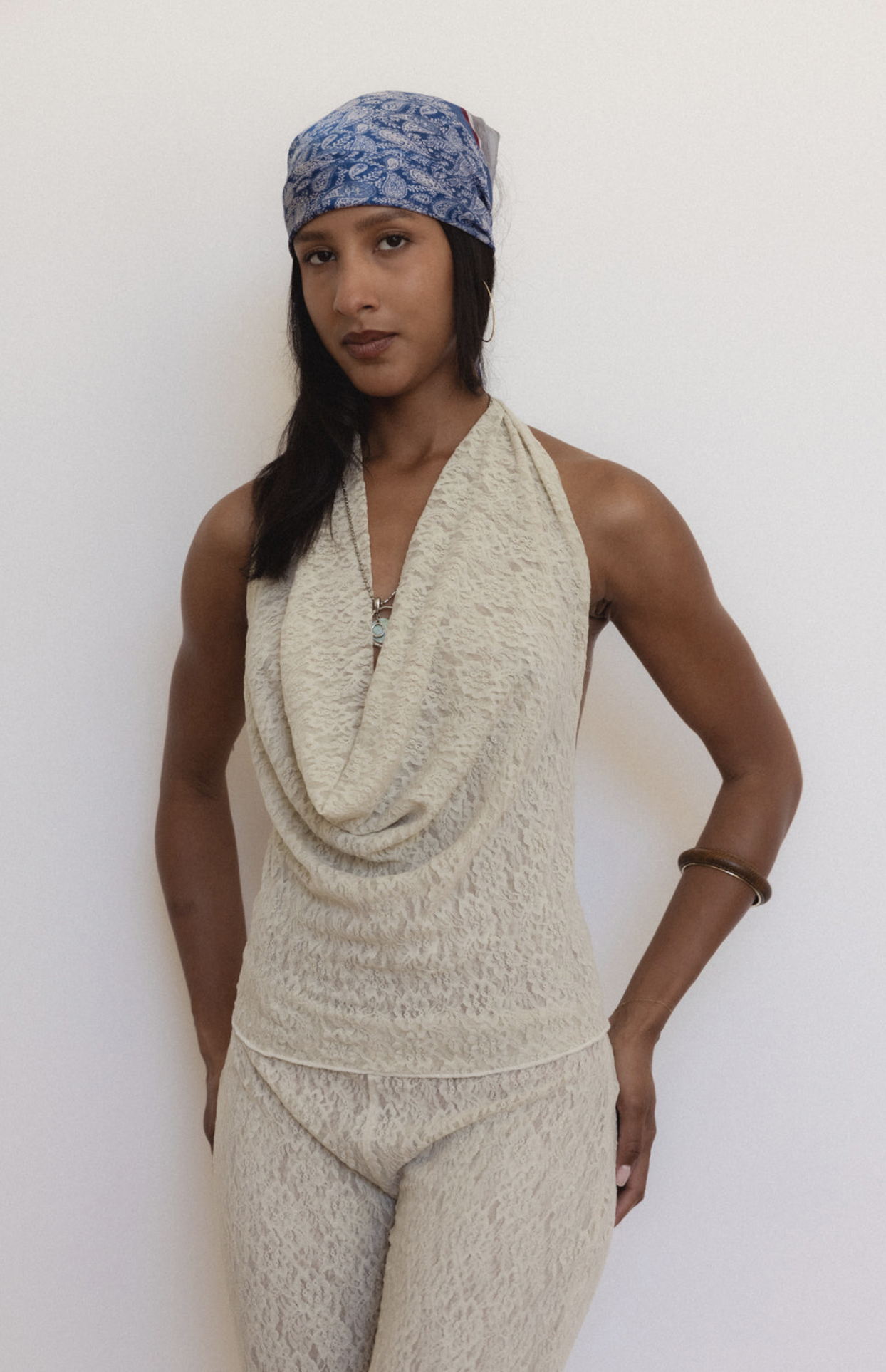 Woman wearing cream textured halter top with cowl neck and matching pants, styled with blue patterned headband