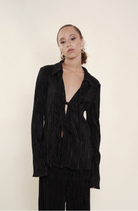 Black pleated velvet tie-front blouse with long sleeves and deep V-neckline worn with matching pants